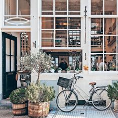 a bicycle parked in front of a building with lots of windows and potted plants