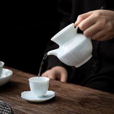 a person pouring water into a cup on top of a wooden table