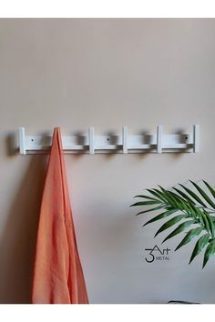 a white coat rack on the wall next to a potted plant and an orange towel