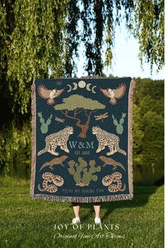 a woman standing in front of a tree holding up a blanket with animals on it