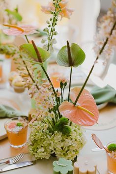 an arrangement of flowers and greenery on a table set for a formal dinner party