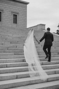 a bride and groom walking up some steps holding each other's hand in black and white