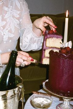 a woman is decorating a cake on a table with wine bottles and silverware