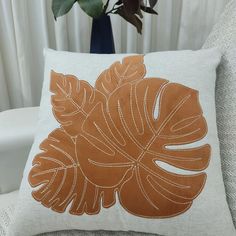 a white couch with a brown and tan pillow on it next to a potted plant