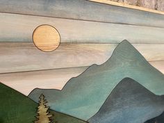 a wooden wall hanging with mountains, trees and a sun in the sky above it