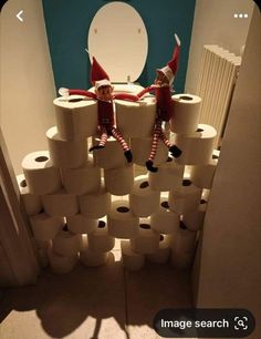 two elfs are sitting on top of toilet paper in the middle of a room