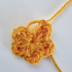 an orange crochet flower on a white surface with yellow yarn in the middle