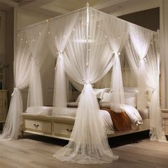 a white canopy bed with sheer curtains and lights