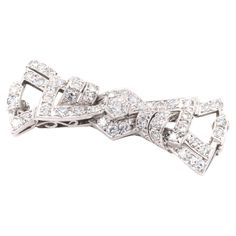 An Art Deco palladium and diamond brooch, comprising one large round brilliant cut diamond, forty-four smaller single cut diamonds, set in palladium, with palladium pin and fittings. This brooch is designed as a stylised bow. A late Art Deco take on a classic bow brooch, with striking angles and well-thought openwork – a highly coveted piece. The brooch is set to the centre with the largest diamond, a round brilliant cut, which is elegantly set within a hexagonal setting, complete with millegrain edging. Two sets of 3 diamonds are set above and below, within chevron shapes, allowing the central diamond to appear as if it were surrounded by another hexagon. Angular diamond set sections sweep out from the centre, interjected by curved lines of diamonds, creating the stylised ‘ears’ of the bo Late Art, Bow Brooch, Diamond Brooch, Curved Lines, Diamond Set, Round Brilliant Cut Diamond, Brilliant Cut Diamond, Makers Mark, Round Brilliant