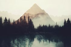 the mountains are reflected in the still water on the lake's surface, with pine trees at the bottom