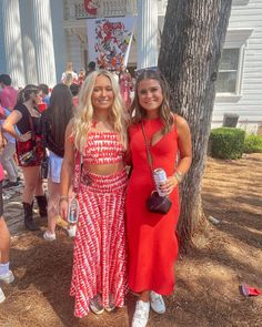 two young women standing next to each other in front of a building with people around