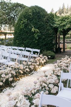 white chairs are lined up in the middle of a flowered area with flowers and greenery