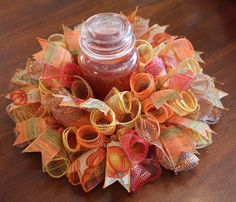 an orange, yellow and red wreath with a jar filled with something on top of it