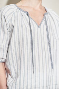 a woman with short hair wearing a white and grey striped shirt, silver necklace and earrings