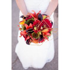 a woman in a white dress holding a red and orange bouquet on her wedding day