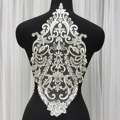 a black mannequin with white and silver designs on it's back, standing in front of a curtain