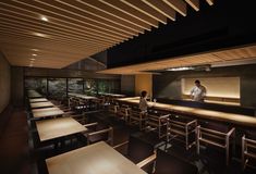 two people are standing at the counter in a restaurant with wooden tables and chairs around them