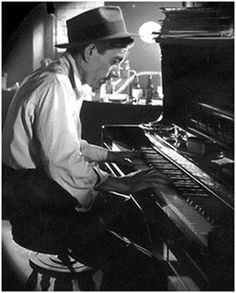 a man sitting at a piano in front of a black and white photo with the caption