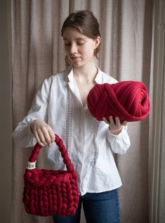 a woman holding a red purse and ball of yarn