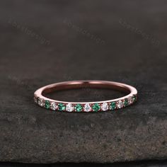 a rose gold band with emerald and white diamonds on the side, sitting on top of a rock