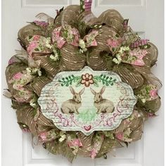 a wreath with two bunnies on it hanging from the front door, decorated with pink and green flowers