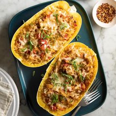 two spaghetti stuffed squash halves on a tray with a fork and bowl of seasoning next to it