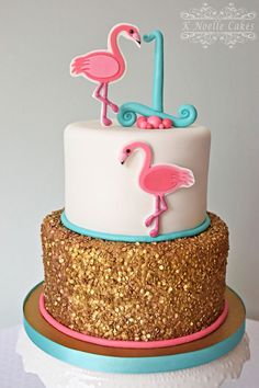 a white and blue cake with pink flamingos on it's top, gold sequins around the edges