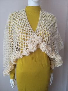 a white crocheted shawl with flowers on the top and bottom, sitting on a mannequin