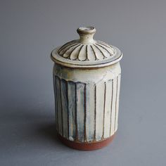 a white and brown ceramic container on a gray surface with a lid in the shape of a ribbed