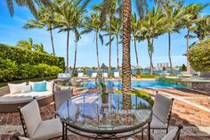 an outdoor dining area with palm trees and water in the background, surrounded by stone patio furniture