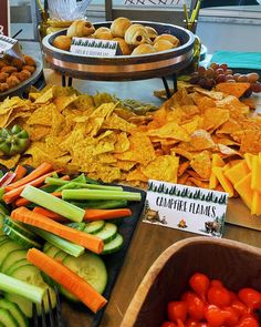 various types of vegetables and fruits on display at a buffet table with corn chips, tomatoes, cucumbers, celery, carrots