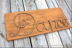 a wooden sign with the word dance written in rope on it's side, sitting on wood planks