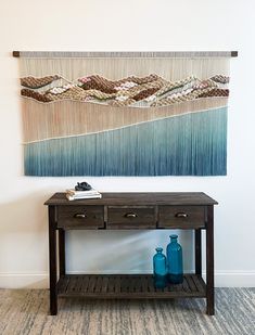 a wooden table with two blue vases on it and a wall hanging behind it