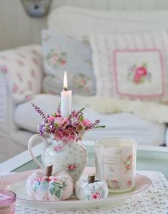 a tea set with flowers and candles on a table in front of a white couch