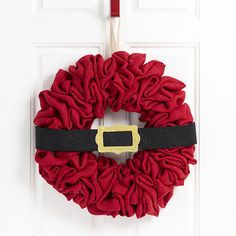 a red and black wreath hanging on a white door with a gold buckle around it