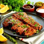 two pieces of meat on a plate with lemons and parsley next to it