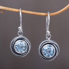 Featuring an original design by Indonesian artisan Wirabhuwana this pair of dangle earrings features two carats of round blue topaz stones. The stones are framed by handcrafted rope motifs in sterling silver that coil around. Blue Round Topaz Earrings, Fine Jewelry Blue Topaz Round Earrings, Blue Topaz Round Earrings, Aquamarine Round Jewelry With Matching Earrings, Blue Topaz Dangle Earrings Fine Jewelry, Pierced Blue Topaz Dangle Jewelry, Round Topaz Earrings For Anniversary, Light Blue Topaz Gemstone Earrings, Blue Topaz Birthstone Round Earrings