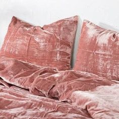 an unmade bed with pink velvet sheets and pillows on top of it, in front of a white wall