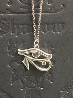 Embrace the power and mystique of ancient Egyptian symbolism with this exquisite Eye of Horus necklace. Available with either a 16-inch black cord featuring a 2-inch extension or a stainless steel chain, this necklace offers versatility and style to suit any preference. Pair it with our matching Eye of Horus earrings for a complete, coordinated look. The Eye of Horus, symbolizing protection, royal power, and good health, adds a touch of historical significance and spiritual meaning to your jewelry collection. Whether you choose the sleek black cord or the durable stainless steel chain, this necklace is perfect for everyday wear or special occasions. Features: Eye of Horus pendant Choice of 16-inch black cord with 2-inch extension or stainless steel chain Matching Eye of Horus earrings avai Eye Of Horus Pendant, Symbolic Jewelry With Adjustable Chain, Symbolic Ankh Necklace Adjustable, Symbolic Ankh Necklace, Adjustable Symbolic Engraved Necklace, Symbolic Engraved Adjustable Necklace, Symbolic Pendant Charm Necklace, Horus Necklace, Eye Of Horus Necklace