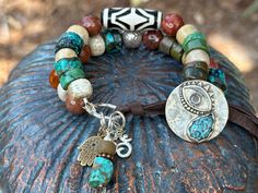 "This Third Eye bracelet is rich in symbolism. It features a Sterling button with a 3rd eye and Turquoise teardrop that doubles as the button closure.  In this two strander, I used Natural Turquoise wheels,  Fossil Coral and beautiful faceted Carnelian beads. One strand showcases a Indian Dzi bead bringing protection and positive energy to the wearer.  A Sterling \"Om\" and a \"Hamsa\" charm dangle from the link bringing their own positive vibe together. Loop the dark brown leather through the button to close.   When you purchase, please note your wrist size.  I will adjust to assure a perfect fit!" Hamsa Charm, Making Stuff, Boho Style Jewelry, 3rd Eye, Yoga Bracelet, Carnelian Beads, Fossil Coral, Boho Accessories, Eye Bracelet