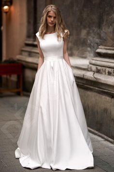 a woman in a white wedding dress standing on the street with her hands behind her back