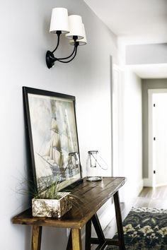 a wooden table topped with a lamp next to a wall mounted painting on a white wall