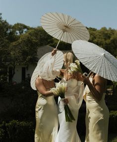 three bridesmaids with umbrellas in their hands and one is holding a bouquet