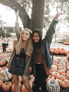 two girls standing next to each other in front of pumpkins