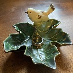 a ring sits on top of a leaf shaped dish with a bird perched on it