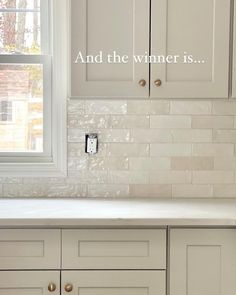 a kitchen with white cabinets and tile backsplashing that says and the winner is