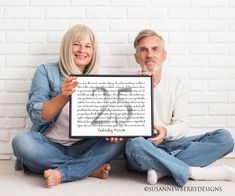 a man and woman sitting on the floor holding up a framed letter