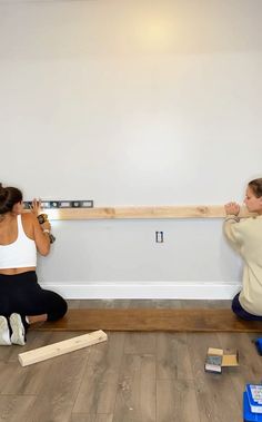 two women are sitting on the floor working on a wall mounted project with wood planks