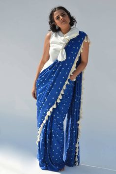 Feminine and charming, this hand tie and dye bandhej pre-draped saree is a fashion statement that will make heads turn.Made in soft cotton satin.It is highlighted with boho tassels.The saree comes with a white shirt with a tie up bow detail.It has an elasticated back waist and a welt pocket for an added comfort. Pre Draped Saree, Boho Tassels, Draped Saree, Cotton Saree Designs, Drape Saree, Hand Tie, Couture Embroidery, Saree Blouse Designs Latest, Bow Top