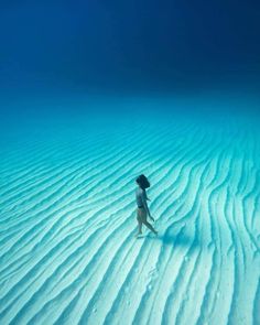 a woman standing on top of a sandy beach next to the ocean under blue water